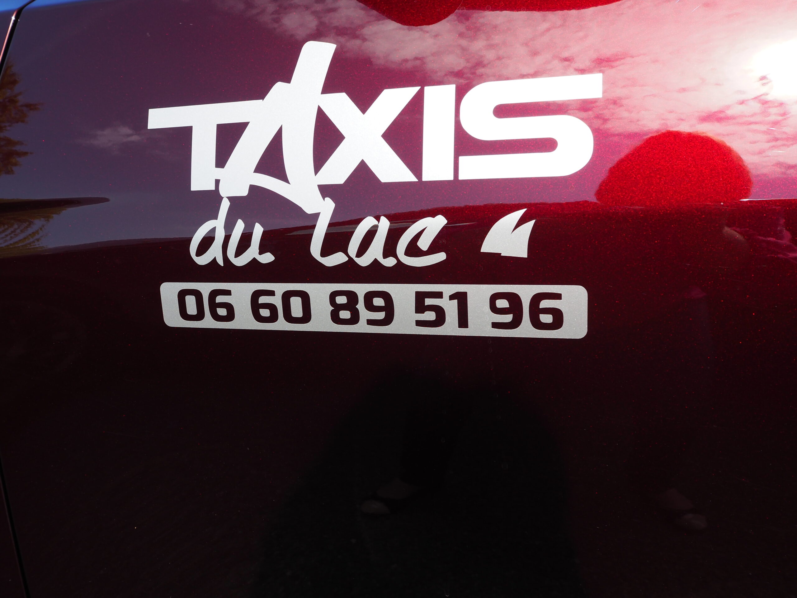 Logo "Taxi du Lac" sur la portière d’une Tesla rouge Logo Taxi du Lac sur la portière de la Tesla rouge